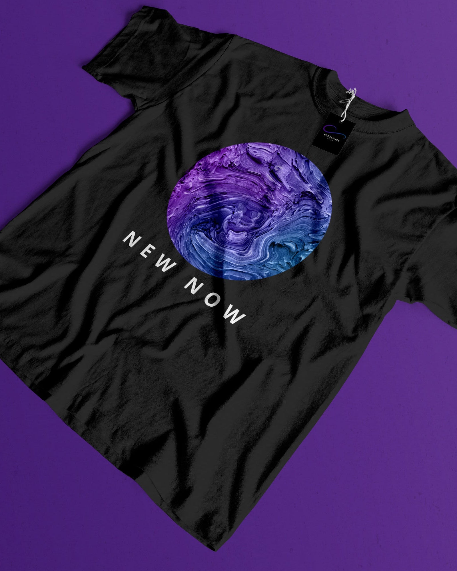 A black short-sleeve t-shirt laid flat on a solid purple background, featuring a circular graphic with a purple and blue marbled design and the text 'NEW NOW' printed below it.