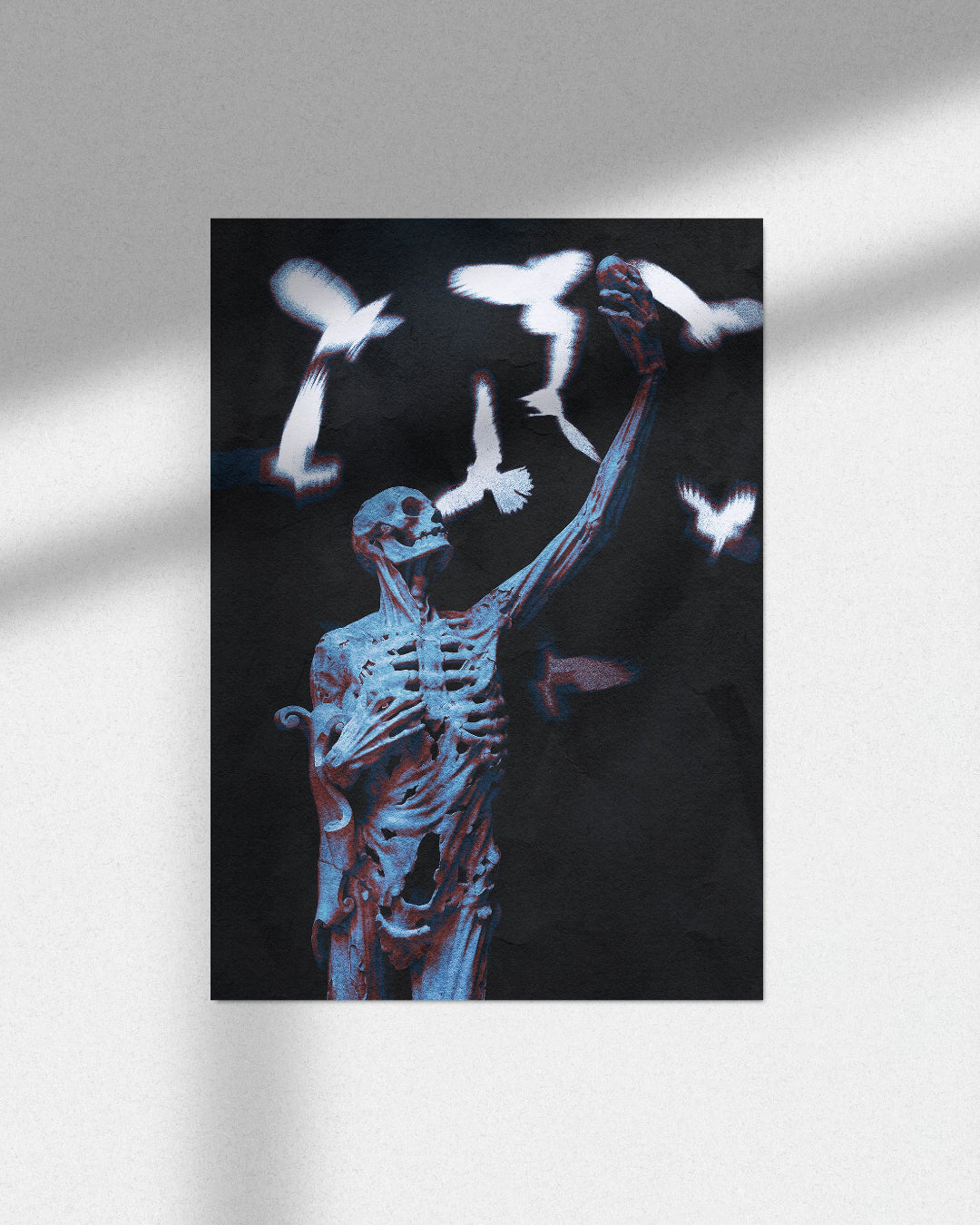 A vertical art print featuring a blue-toned skeleton figure reaching upward among white doves against a black background, displayed on a light gray wall with soft window-light shadows.